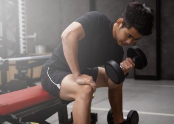 Whey protein - homem sentado na academia levantando halter