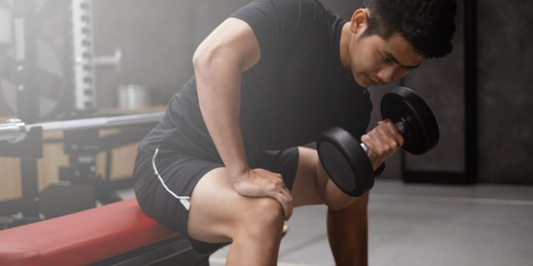 Whey protein - homem sentado na academia levantando halter