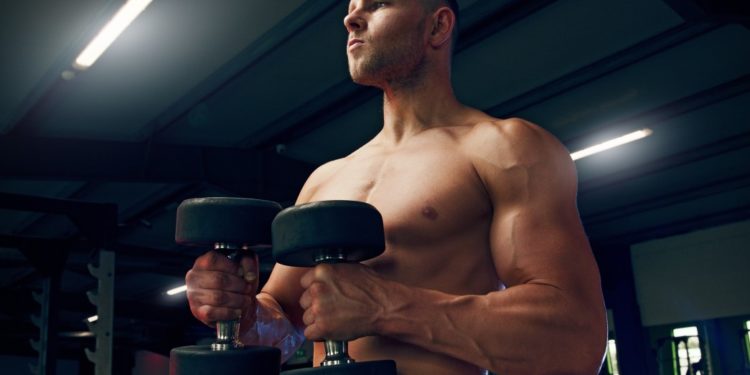 Suplemento BCAA, homem levantando halteres na academia sem camisa