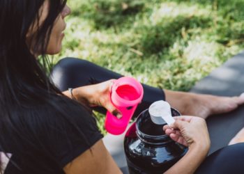 Mulher preparando seu pré-treino, colocando um scoop de pré-treino na coqueteleria.