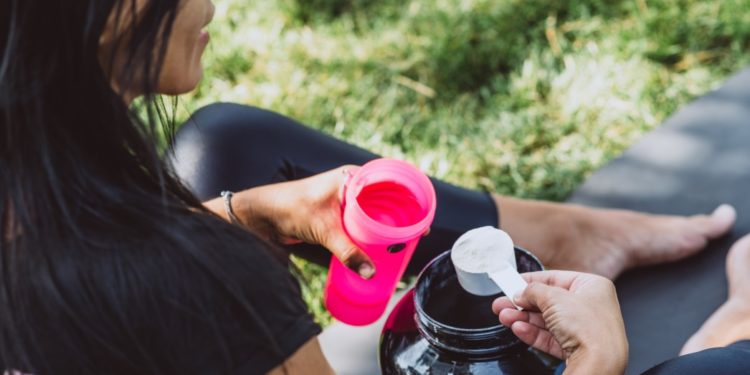 Mulher preparando seu pré-treino, colocando um scoop de pré-treino na coqueteleria.
