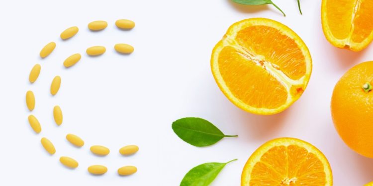 Comprimidos laranjas de vitamina c, formando um c, e metade uma laranja