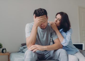 tadalafila - homem sentado na cama com a mão na cabeça, mulher consolando apoiada no ombro dele