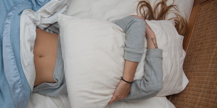 dor de barriga - menina deitada abraçada com travesseiro